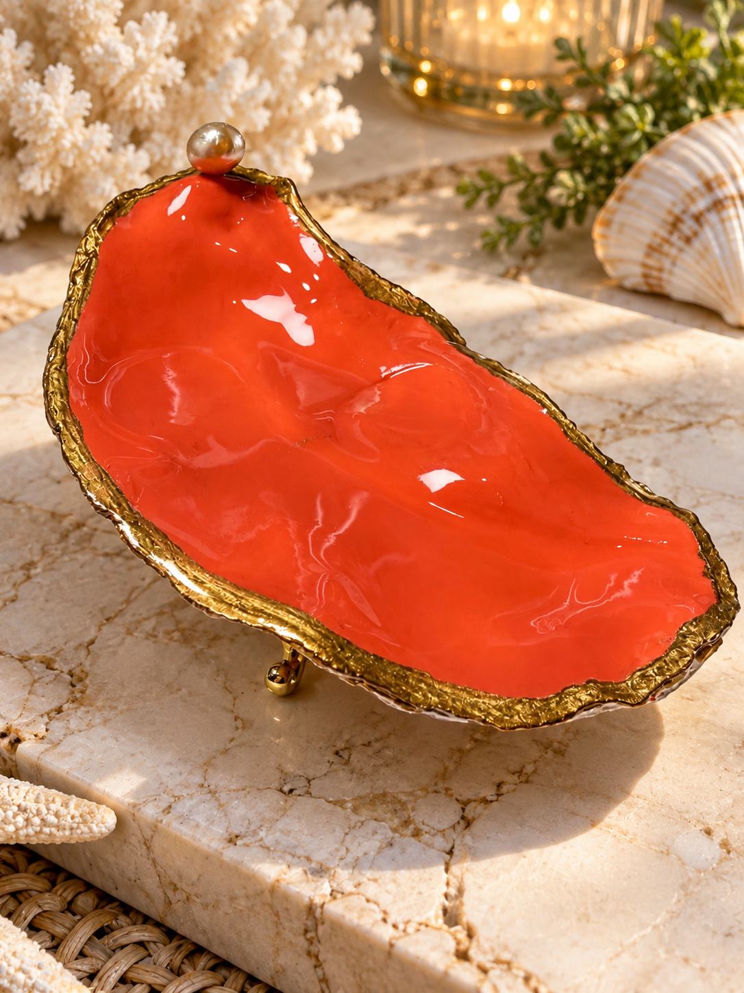 Coral-orange decorative oyster shell with gold-toned edges and a pearl-like accent
