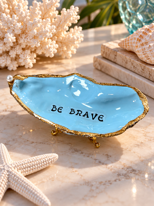 Sky-blue decorative oyster shell with Be Brave lettering and gold-toned edges